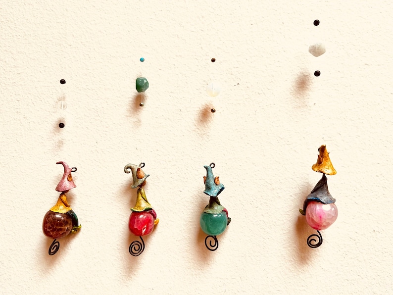 May include: Five whimsical figurines with colorful hats and gemstone accents. Each figurine is made of clay and has a unique design. The figurines are hanging from the ceiling.