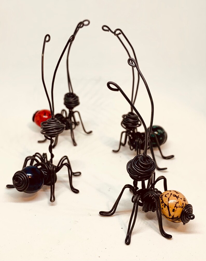 Puede incluir: Cuatro hormigas artesanales de alambre con cuerpos de cuentas de vidrio en rojo, verde, azul y beige. Las hormigas tienen cuerpos de alambre enrollado, seis patas de alambre y antenas largas y curvas. Esculturas &uacute;nicas.