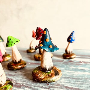Puede incluir: Una colecci&oacute;n de figuritas de setas en miniatura pintadas a mano. Las setas est&aacute;n hechas de arcilla y tienen sombreros de diferentes colores con tallos y bases blancas. Los sombreros est&aacute;n decorados con lunares y las bases est&aacute;n pintadas con una variedad de colores.