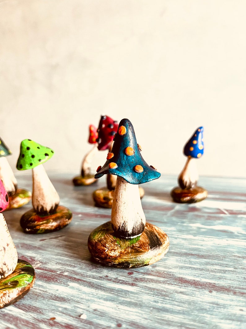 Puede incluir: Una colecci&oacute;n de figuritas de setas en miniatura pintadas a mano. Las setas est&aacute;n hechas de arcilla y tienen sombreros de diferentes colores con tallos y bases blancas. Los sombreros est&aacute;n decorados con lunares y las bases est&aacute;n pintadas con una variedad de colores.