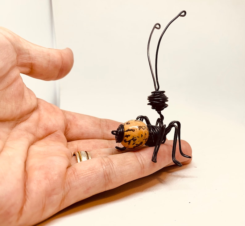Puede incluir: Una escultura de alambre hecha a mano de una hormiga. La hormiga tiene un cuerpo marr&oacute;n y beige, patas de alambre negro y antenas. La escultura es una obra de arte &uacute;nica.