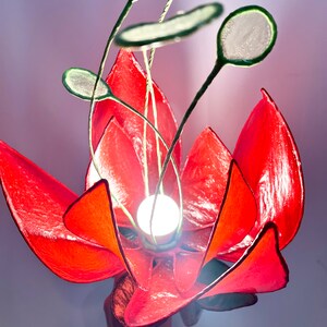 Puede incluir: Una l&aacute;mpara de papel con forma de flor roja con tallos y hojas verdes. La l&aacute;mpara tiene una bombilla blanca en el centro.