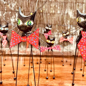 Puede incluir: Un grupo de figuritas de gatos negros con patas largas y delgadas y pajaritas rojas con lunares blancos. Los gatos tienen ojos verdes y est&aacute;n de pie sobre una superficie de madera.