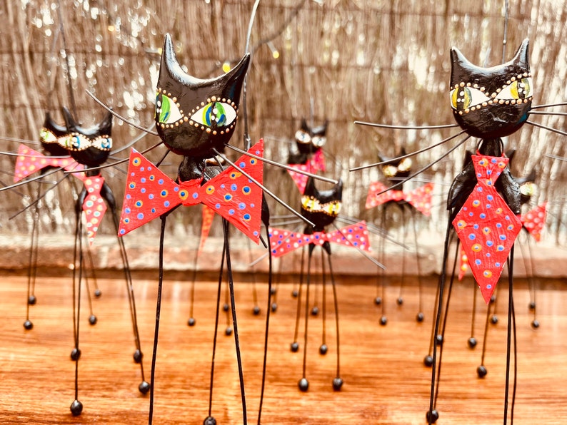 Puede incluir: Un grupo de figuritas de gatos negros con patas largas y delgadas y pajaritas rojas con lunares blancos. Los gatos tienen ojos verdes y est&aacute;n de pie sobre una superficie de madera.
