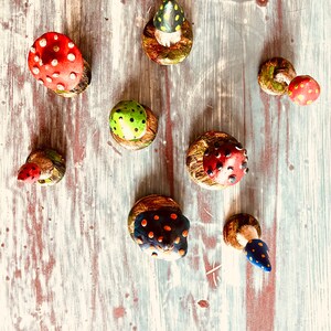 Puede incluir: Una colecci&oacute;n de ocho setas de cer&aacute;mica pintadas a mano con varios colores y patrones. Las setas se muestran sobre una superficie de madera blanca.