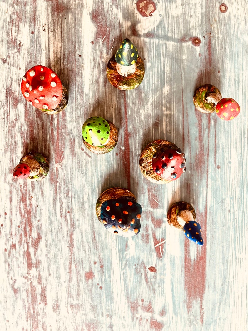 Puede incluir: Una colecci&oacute;n de ocho setas de cer&aacute;mica pintadas a mano con varios colores y patrones. Las setas se muestran sobre una superficie de madera blanca.