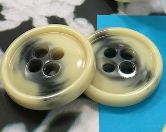 May include: Five off-white buttons with black swirl designs and four holes each. The buttons are on a white lace background and a blue surface.