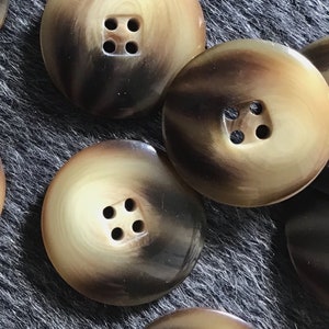 May include: A collection of ten brown and cream coloured buttons with four holes each. The buttons are made of a mottled material that resembles tortoiseshell.
