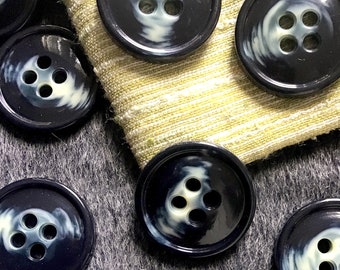 May include: A collection of ten dark blue buttons with a white swirl design and four holes each. The buttons are arranged on a gray and beige fabric background.