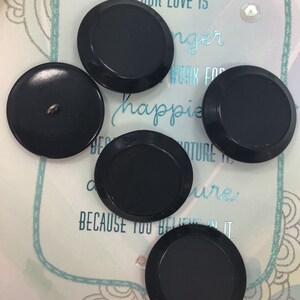 May include: Four black plastic buttons with a raised edge. The buttons are round and have a smooth surface.