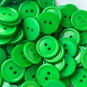 May include: A large pile of bright green plastic buttons with two holes each. The buttons are all the same size and shape.
