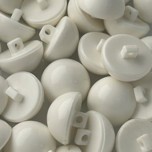 May include: A pile of white plastic dome-shaped buttons with two holes and a shank on the back.