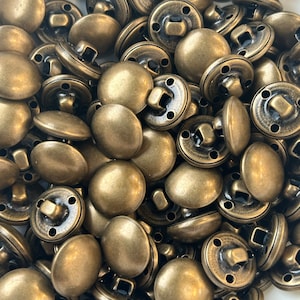 May include: A large pile of antique gold-toned metal buttons. The buttons are round and have a raised center. They have four holes around the edge and a small metal loop on the back.