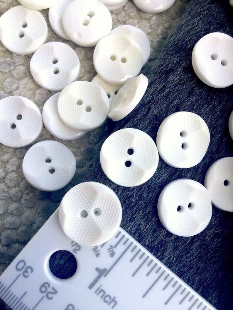 May include: A collection of white plastic buttons with two holes each. The buttons have a textured surface and are approximately 1 inch in diameter.
