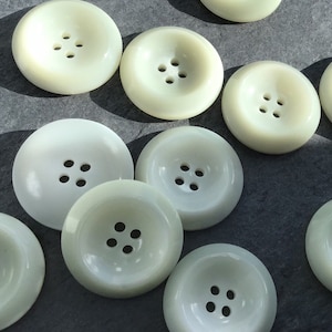 May include: A collection of ten off-white plastic buttons with four holes each. The buttons are round and have a raised center.