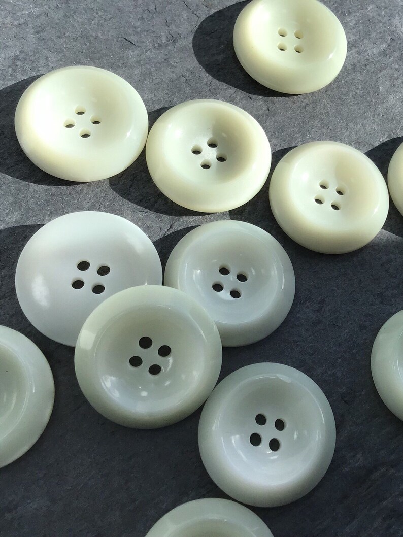 May include: A collection of ten off-white plastic buttons with four holes each. The buttons are round and have a raised center.