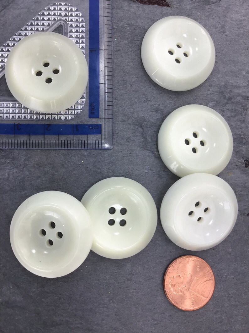 May include: Five white plastic buttons with four holes each. The buttons are approximately 1 inch in diameter.