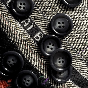 May include: Close-up of black buttons with four holes each, arranged in a row on a black and white patterned fabric.