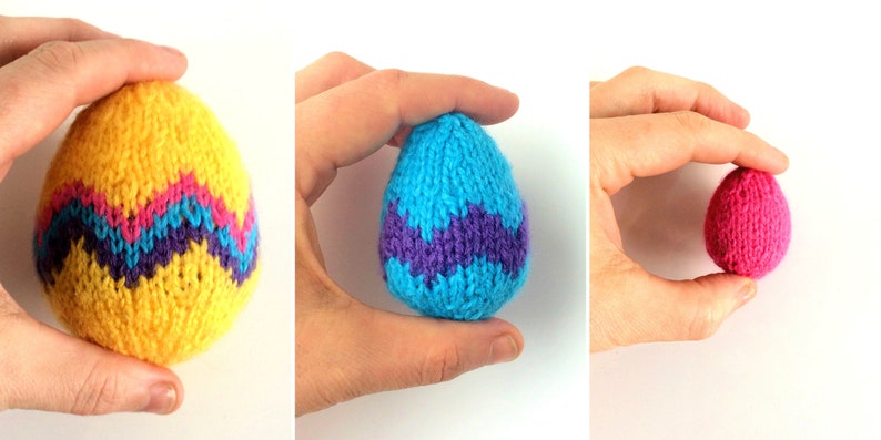 May include: Three knitted egg-shaped decorations in varying sizes. The largest is yellow with a blue and pink chevron pattern. The medium egg is light blue with a purple chevron pattern. The smallest egg is solid pink with a textured knit finish.
