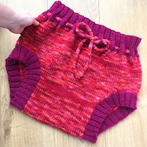 May include: Red and pink striped knitted baby bloomers with a pink drawstring.