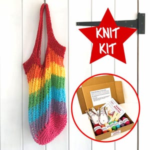 May include: A rainbow-coloured mesh tote bag hanging vertically, paired with a cardboard craft kit box containing yarn skeins, circular knitting needles, and printed instructions. A red star graphic with the white text KNIT KIT is visible.