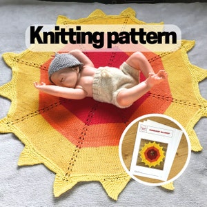 May include: A circular knitted blanket featuring a sunburst design in yellow, orange, and red with a lace border. A doll wearing a gray hat and beige shorts lies on the blanket. A printed document titled "SUNBURST BLANKET" is included.