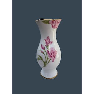 May include: A white porcelain vase with a flared rim and a rounded body, featuring a painted design of pink rose blossoms, buds, and green leaves. The rim and the base of the vase are accented with a thin, metallic gold trim detail.