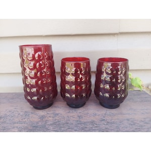 Könnte beinhalten: Set aus drei roten Glasbechern mit einer Blasenstruktur. Die Becher sind in verschiedenen Größen.