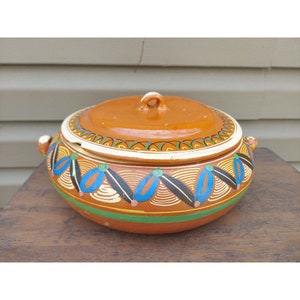 May include: A brown ceramic casserole dish with a lid, featuring hand-painted blue, green, yellow, and black geometric designs.