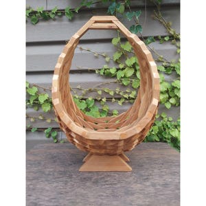 May include: A wooden fruit bowl with a unique, woven design. The bowl is shaped like an egg and has a stand.