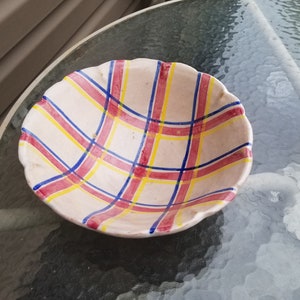 Op de afbeelding: Een keramische kom met een gegolfde rand en een geruit patroon in tinten roze, geel, blauw en wit.