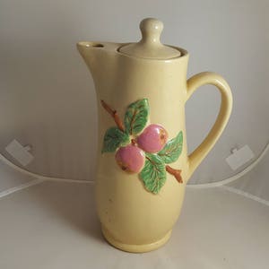 Può includere: Un'anfora in ceramica gialla con coperchio, con un design dipinto a mano di mele rosa e foglie verdi su un ramo.