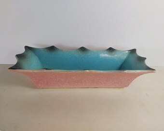 May include: A pink and blue ceramic planter with a scalloped edge. The planter has a speckled glaze and a unique shape.