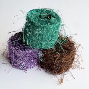 May include: Three spools of yarn in different colors: teal, purple, and brown. The yarn is fluffy and has a fuzzy texture.