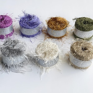May include: Seven spools of fluffy yarn in various colors, including purple, lavender, gold, green, silver, white, and beige. Each spool is labeled "Flutter".