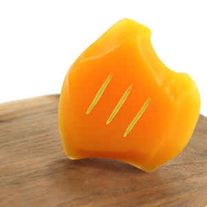 May include: A bright orange, irregularly shaped bar of soap with three thin lines carved into it. The soap is sitting on a wooden surface.