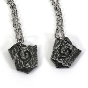 May include: Two silver necklaces with matching pendants. Each pendant is a silver, textured, shield-shaped piece with a stylized, swirling design.