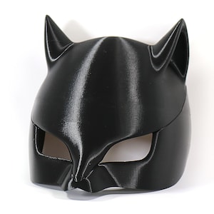 May include: A black plastic cat mask with pointy ears and eye holes. The mask is smooth and has a glossy finish.