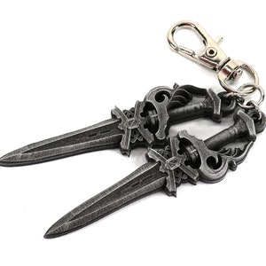 May include: A keychain featuring two decorative, antique-style daggers with ornate handles and a silver-colored clasp. The daggers are a dark, metallic gray color and have detailed designs.