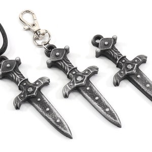 May include: Three silver-colored dagger pendants, one on a black cord, one on a silver key chain, and one on a silver chain. The daggers have a detailed design with a cross-shaped handle and a pointed blade.