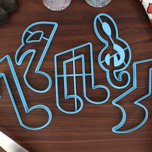 May include: A set of five blue plastic cookie cutters shaped like musical notes. The cutters are on a wooden surface.