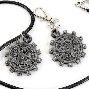 May include: Two silver-toned pendants with intricate designs, one on a black cord necklace and the other on a silver chain with a lobster clasp. The pendants feature a circular design with a central triangle and various symbols.