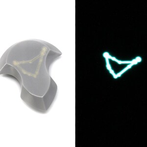 May include: A gray ceramic tile with a white outline of the constellation Capricorn. The tile glows green in the dark.