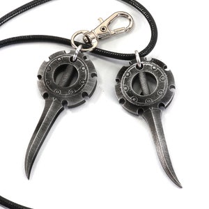May include: A pair of silver-toned metal pendants with a circular design and a pointed blade hanging from a black cord with a silver clasp.