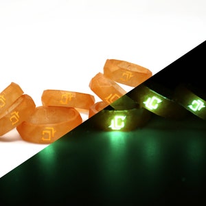 May include: A set of six orange glow-in-the-dark rings with a unique design. The rings are stacked on top of each other and glow green in the dark.