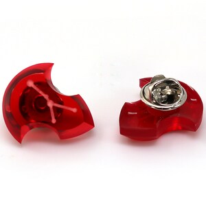 May include: Two red plastic pins shaped like a crescent moon with a white design in the center. One pin has a silver clasp on the back.
