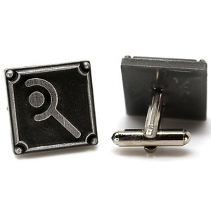 May include: Pair of square cufflinks with a magnifying glass design. The cufflinks are dark gray with a silver-colored post and backing. Each cufflink has a magnifying glass symbol in the center of the square.