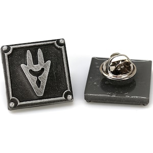 Op de afbeelding: Een zilveren metalen pin met een zwart vierkant ontwerp met een gestileerd drietandsymbool. De achterkant van de pin heeft een standaard pinrug.
