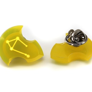 Op de afbeelding: Gele emaille pin met een sterrenbeeld ontwerp. De pin heeft een zilveren metalen sluiting aan de achterkant.