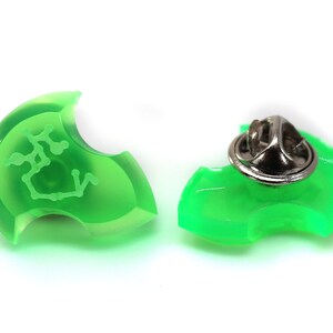 May include: A green plastic pin with a silver pin back. The front of the pin has a white outline of a constellation.
